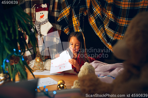 Image of Merry Christmas and Happy Holidays. Cute little child girl writes the letter to Santa Claus near Christmas tree