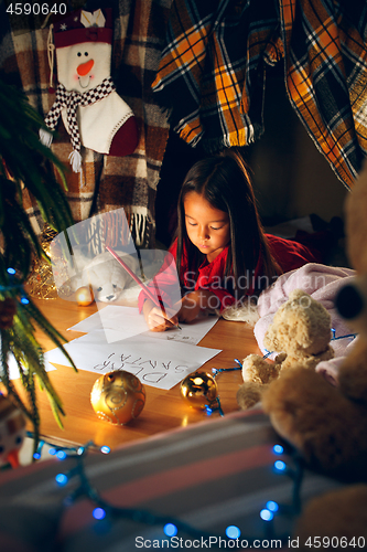 Image of Merry Christmas and Happy Holidays. Cute little child girl writes the letter to Santa Claus near Christmas tree