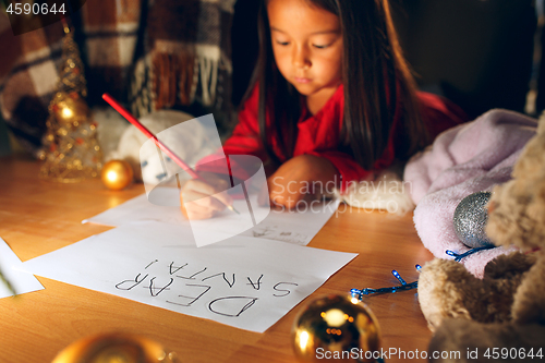 Image of Merry Christmas and Happy Holidays. Cute little child girl writes the letter to Santa Claus near Christmas tree