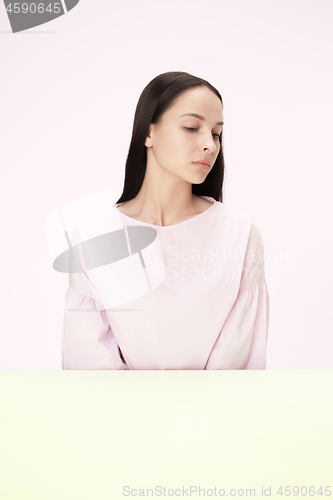 Image of Serious business woman sitting at a table on a pink background