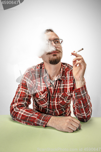 Image of Handsome hipster man smoking cigarette at home. Man looking upwards and enjoying spending free time.