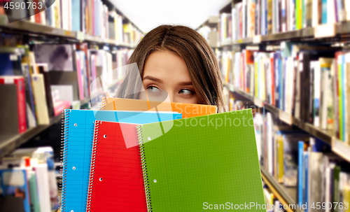 Image of teenage student girl behind notebooks at library