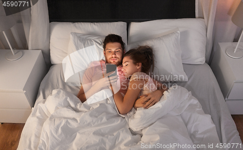 Image of man using smartphone while girlfriend is sleeping