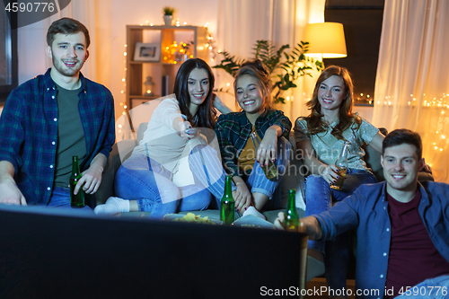 Image of happy friends with drinks watching tv at home