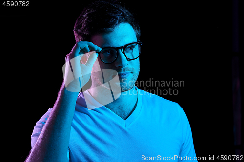 Image of man in glasses over neon lights in dark room