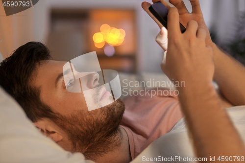 Image of young man with smartphone in bed at night