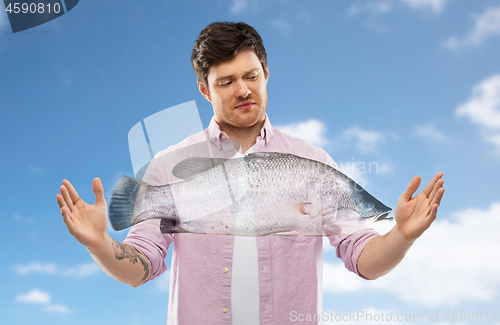 Image of displeased young man showing size of fish over sky