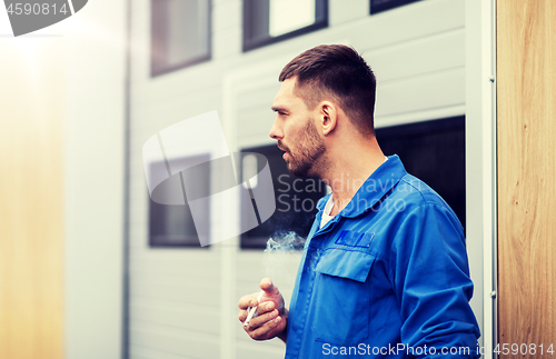 Image of auto mechanic smoking cigarette at car workshop