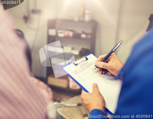 Image of auto mechanic with clipboard and man at car shop