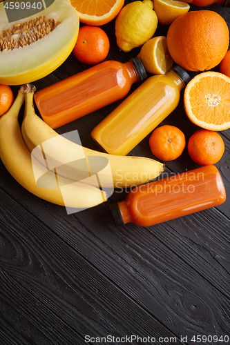 Image of Yellow and orange fruits and botteled juices placed on black woo