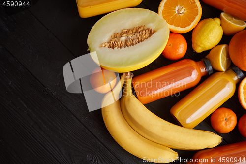 Image of Yellow and orange fruits and botteled juices placed on black woo