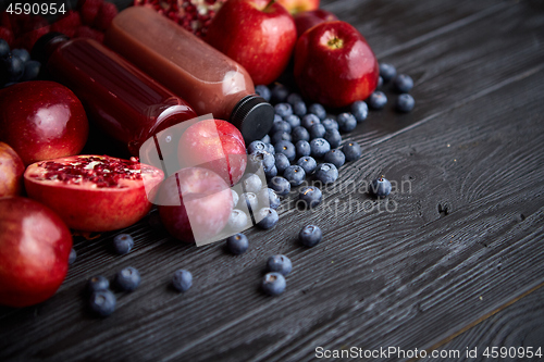 Image of Various fresh red, purple black fruits. Mix of fruits and bottled juices on black