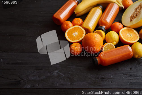 Image of Yellow and orange fruits and botteled juices placed on black woo