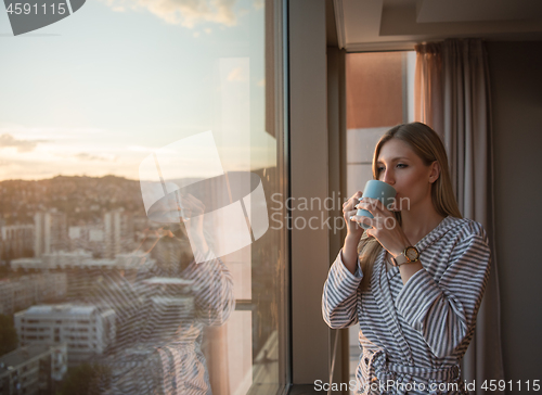 Image of young woman enjoying evening coffee by the window