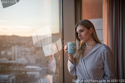 Image of young woman enjoying evening coffee by the window