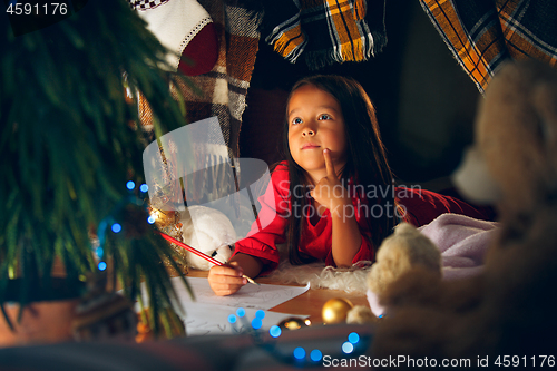 Image of Merry Christmas and Happy Holidays. Cute little child girl writes the letter to Santa Claus near Christmas tree