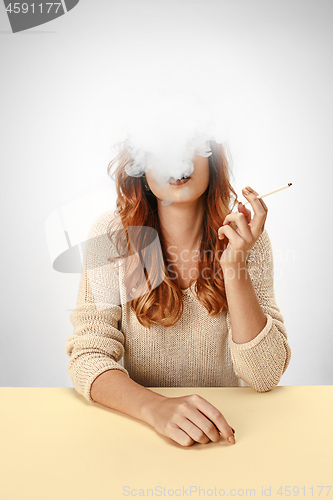 Image of Tranquil woman sitting and smoking resting at the table. Cloud of smoke covering her face. Copy space