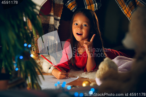 Image of Merry Christmas and Happy Holidays. Cute little child girl writes the letter to Santa Claus near Christmas tree