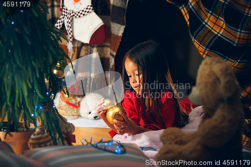 Image of christmas, holidays and childhood concept - happy girl in red clothes decorating natural fir tree