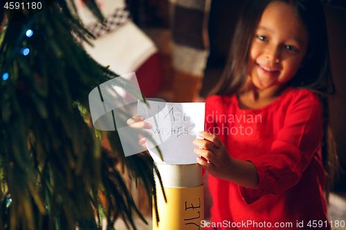 Image of Merry Christmas and Happy Holidays. Cute little child girl writes the letter to Santa Claus near Christmas tree