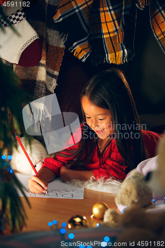 Image of Merry Christmas and Happy Holidays. Cute little child girl writes the letter to Santa Claus near Christmas tree