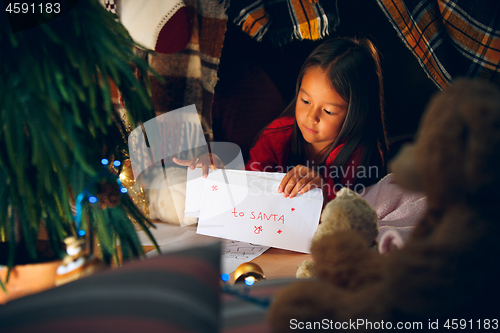 Image of Merry Christmas and Happy Holidays. Cute little child girl writes the letter to Santa Claus near Christmas tree