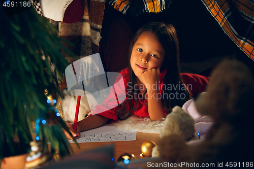 Image of Merry Christmas and Happy Holidays. Cute little child girl writes the letter to Santa Claus near Christmas tree