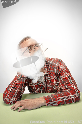 Image of Handsome hipster man smoking cigarette at home. Man looking upwards and enjoying spending free time.