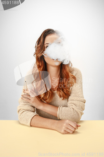 Image of Tranquil woman sitting and smoking resting at the table. Cloud of smoke covering her face. Copy space