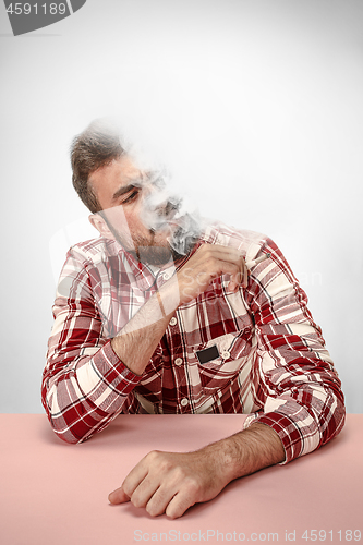 Image of Handsome hipster man smoking cigarette at home. Man looking upwards and enjoying spending free time.