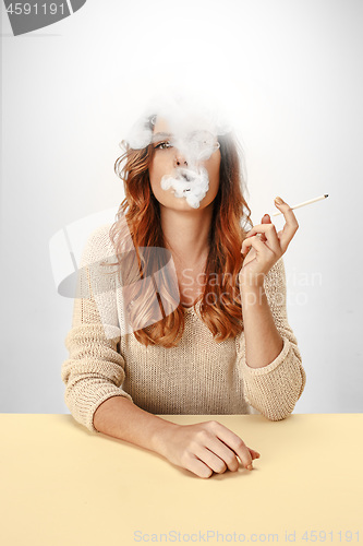 Image of Tranquil woman sitting and smoking resting at the table. Cloud of smoke covering her face. Copy space