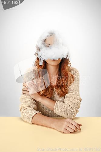 Image of Tranquil woman sitting and smoking resting at the table. Cloud of smoke covering her face. Copy space