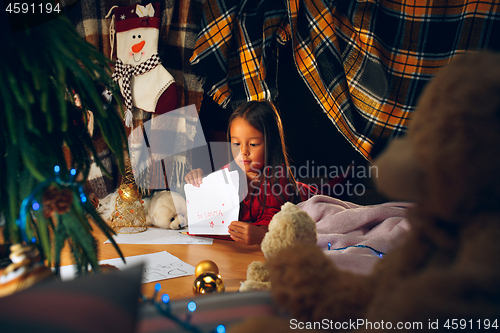 Image of Merry Christmas and Happy Holidays. Cute little child girl writes the letter to Santa Claus near Christmas tree