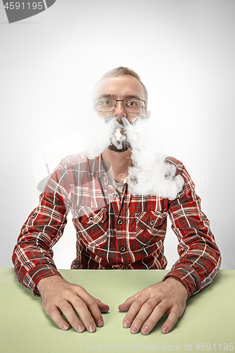 Image of Handsome hipster man smoking cigarette at home. Man looking upwards and enjoying spending free time.