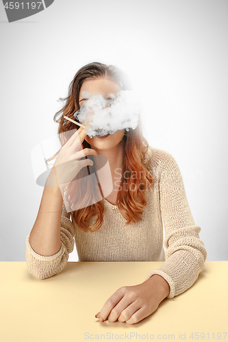 Image of Tranquil woman sitting and smoking resting at the table. Cloud of smoke covering her face. Copy space