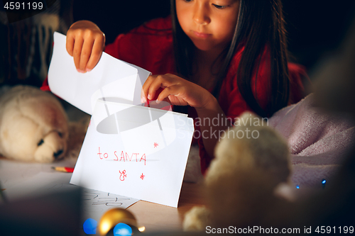 Image of Merry Christmas and Happy Holidays. Cute little child girl writes the letter to Santa Claus near Christmas tree