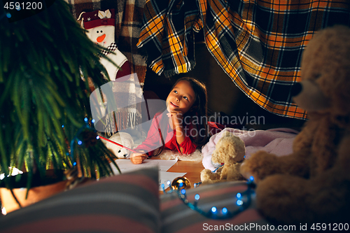 Image of Merry Christmas and Happy Holidays. Cute little child girl writes the letter to Santa Claus near Christmas tree