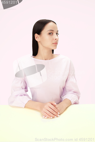 Image of Serious business woman sitting at a table on a pink background