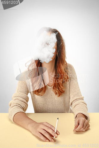 Image of Tranquil woman sitting and smoking resting at the table. Cloud of smoke covering her face. Copy space