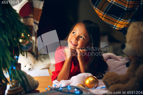 Image of christmas, holidays and childhood concept - happy girl in red clothes decorating natural fir tree