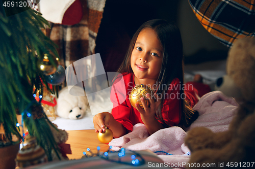 Image of christmas, holidays and childhood concept - happy girl in red clothes decorating natural fir tree
