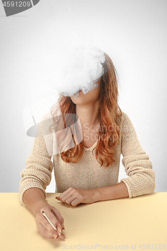 Image of Tranquil woman sitting and smoking resting at the table. Cloud of smoke covering her face. Copy space