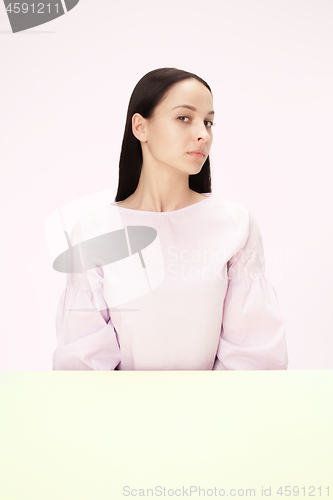 Image of Serious business woman sitting at a table on a pink background