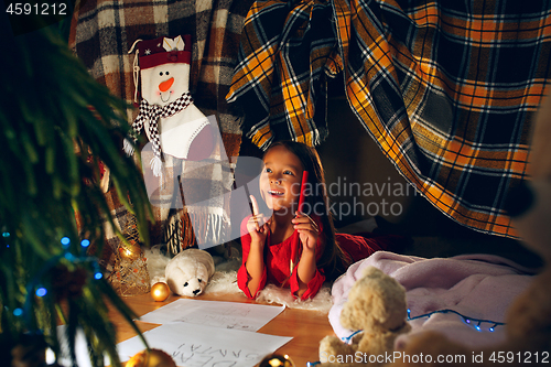 Image of Merry Christmas and Happy Holidays. Cute little child girl writes the letter to Santa Claus near Christmas tree