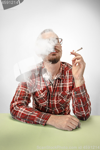 Image of Handsome hipster man smoking cigarette at home. Man looking upwards and enjoying spending free time.