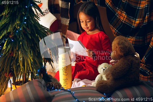 Image of Merry Christmas and Happy Holidays. Cute little child girl writes the letter to Santa Claus near Christmas tree