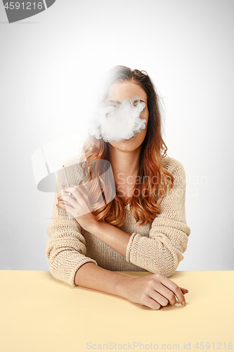 Image of Tranquil woman sitting and smoking resting at the table. Cloud of smoke covering her face. Copy space