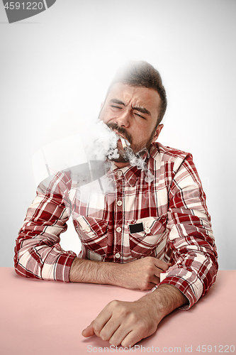 Image of Handsome hipster man smoking cigarette at home. Man looking upwards and enjoying spending free time.