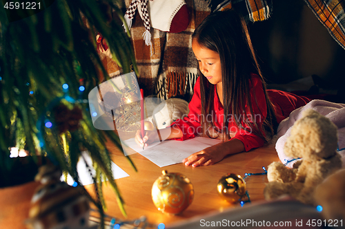 Image of Merry Christmas and Happy Holidays. Cute little child girl writes the letter to Santa Claus near Christmas tree