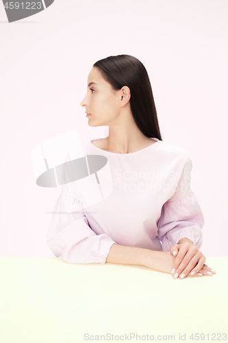 Image of Serious business woman sitting at a table on a pink background